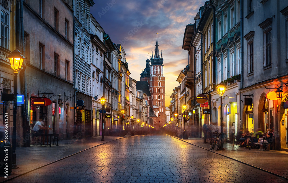 Fototapeta premium Krakow evening view of Florianska Street leading toward St Mary’s Basilica with illuminated historical townhouses, vibrant city life, atmospheric lights, and architectural details of old town Poland