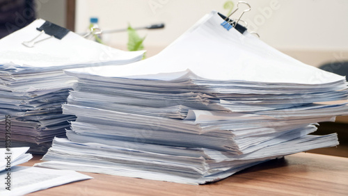 Huge stacks of sorted paper documents with black binder clips on a wooden office desk. Concept of bureaucracy and heavy administrative workload. Photo