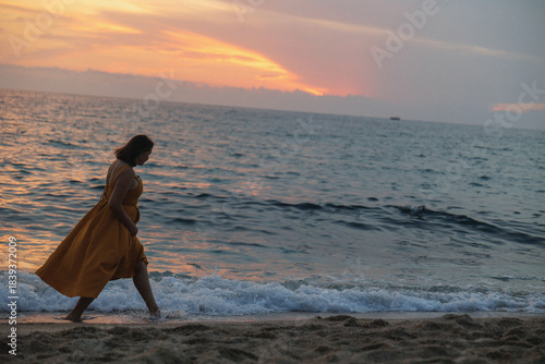 Woman Walking Shoreline Sunset Golden Dress, Waves Lapping At Ankles, Footprints Trailing In Wet Sand, Warm