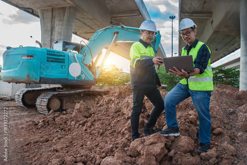Construction Workers Using Digital Tablet at Job Site with Excavator Under Highway Structure