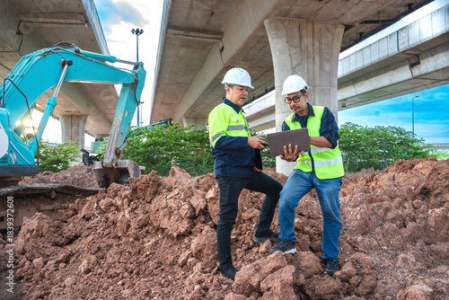 Construction Workers Collaborating on Project Progress Under Overpass with Excavator and Loamy Soil