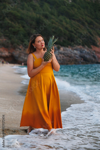 Woman On Beach Holding Pineapple, Wearing Flowing Yellow Dress, Barefoot In Surf, Tropical Cove With Green