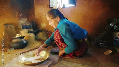An elderly Indian woman aged over seventy prepares food on a traditional stove inside a rural home. The scene reflects village lifestyle, traditional cooking, resilience, and everyday life in India.
