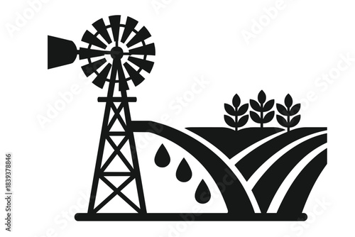 Windmill stands tall next to fields with crops and water drops in a rural landscape during daylight