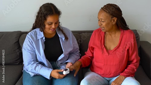 African daughter measuring pulse with oximeter to her mother at home - Healthcare, family and disease concept