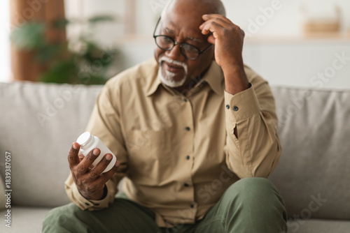 Fotografía An older man sits on a couch, displaying concern as he examines a bottle of medication