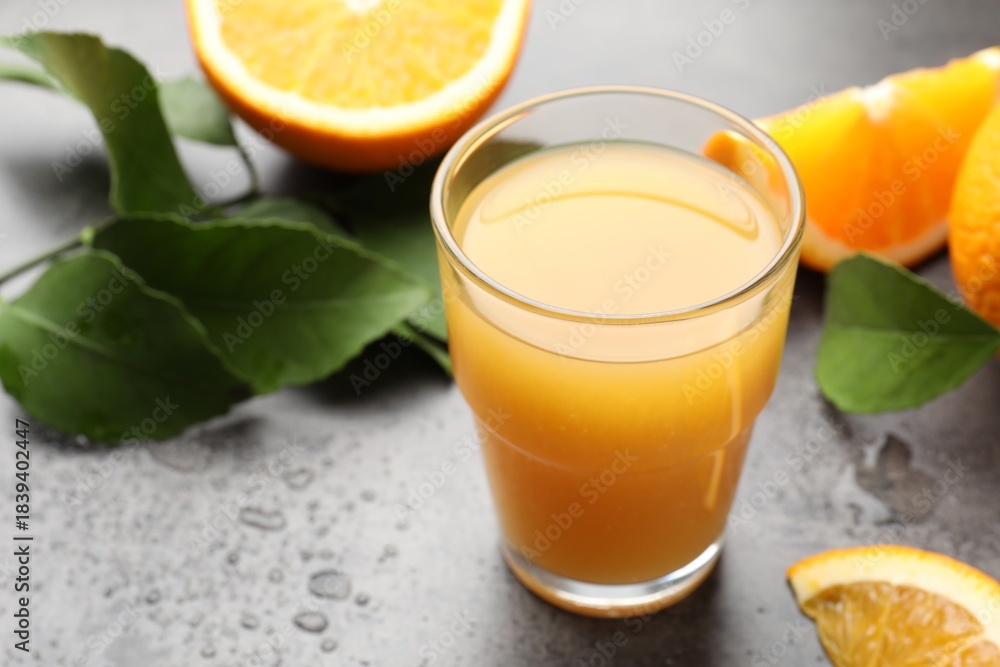Fototapeta premium Fresh orange juice, fruits and leaves on grey table, closeup