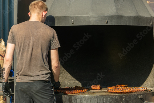 Person grilling ribs on outdoor smoker. Juicy glazed ribs cooking on open smoker with person tending meat during backyard barbecue.