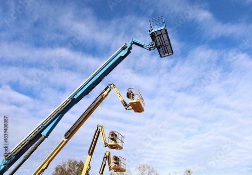 Four aerial working platforms of cherry picker against blue cloudy sky.