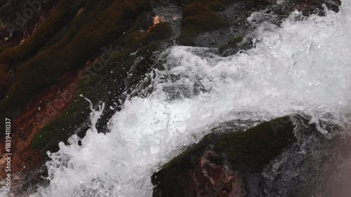 ripresa video laterale e dettagliata, in tempo reale, dell'acqua che scorre impetuoso lungo le pareti rocciose di una cascata di montagna