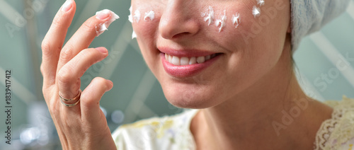 Beautiful Young Woman applying facial moisturizing cream in bathroom.Home interior. Skincare concept