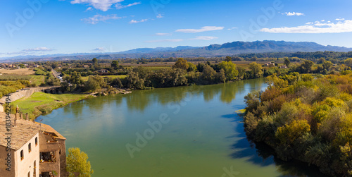 High-angle panoramic view of the Ebro river winding through Miravet, Catalonia, with green vegetation and distant mountains.