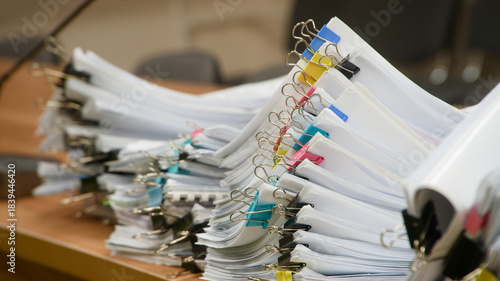 Huge stacks of sorted paper documents with colorful binder clips on a wooden office desk. Concept of bureaucracy and heavy administrative workload. Photo
