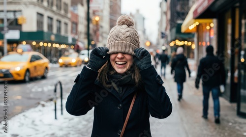 Young woman playing with winter cap on city street 