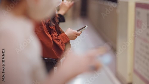 Slow motion close-up of a woman using her smartphone while waiting on a platform at a Japanese metro station. She stands calmly, waiting for her destination.