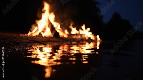 Fiery bonfire reflecting on water at night, sparks flying everywhere.