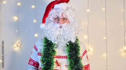 A man dressed as Santa Claus on a white background with festive lights, quietly dancing and enjoying the holiday mood in a playful festive scene.