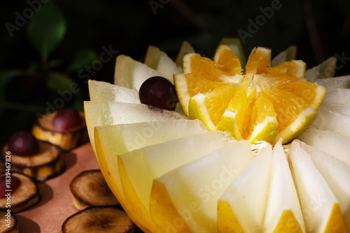 Half a melon and half an orange on top of the melon; the fruits are cut in a sculpted manner.