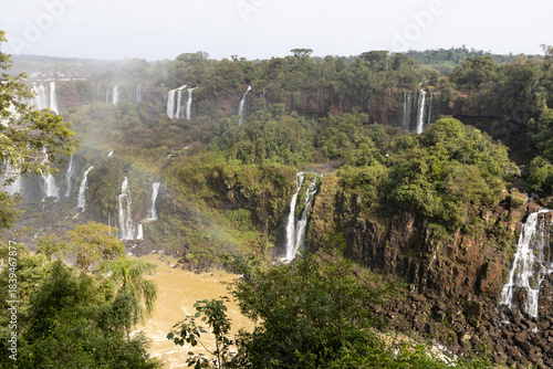 Several small waterfalls cascade down the Iguazu Falls amidst the trees, with a small, gentle rainbow in front of them