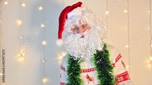 A man dressed as Santa Claus on a white background with festive lights, quietly dancing and enjoying the holiday mood in a playful festive scene.