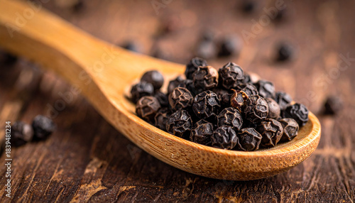 Fototapeta Naklejka Na Ścianę i Meble -  Whole black peppercorns heaped in wooden spoon on rustic wooden surface. Aromatic spice seeds