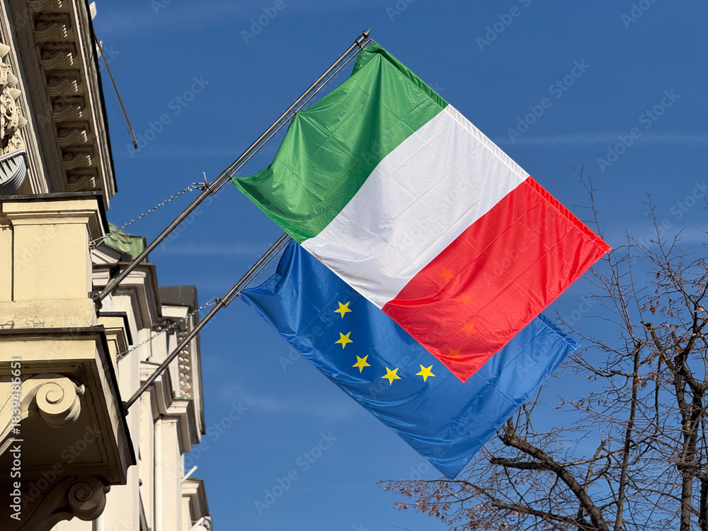 Naklejka premium Italian and European flags close view against clear blue sky. Diplomatic unity, international connection, partnership values and shared cultural identity in modern Europe.