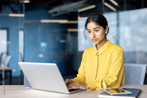 Serious young Indian businesswoman sitting at a desk in the office and working intently on a laptop