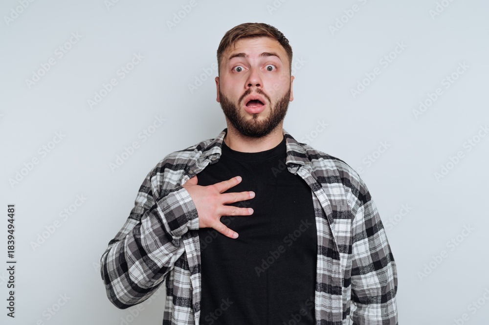 Fototapeta premium A surprised man with a beard and plaid shirt holding his chest.