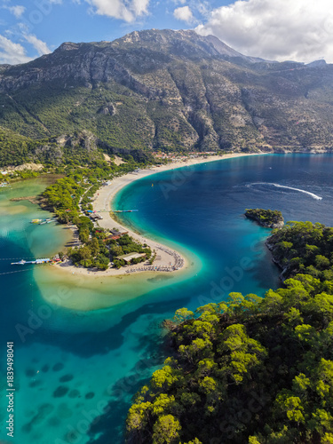 Aerial view of green pine trees, clear turquoise water and mountains in the background in Oludeniz, Turkey. Flying over famous blue lagoon in Oludeniz