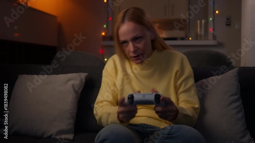 Blonde woman lounging on living room sofa at night, intensely play video game with controller, cycling from concentration and frustration to joyful celebration after victory