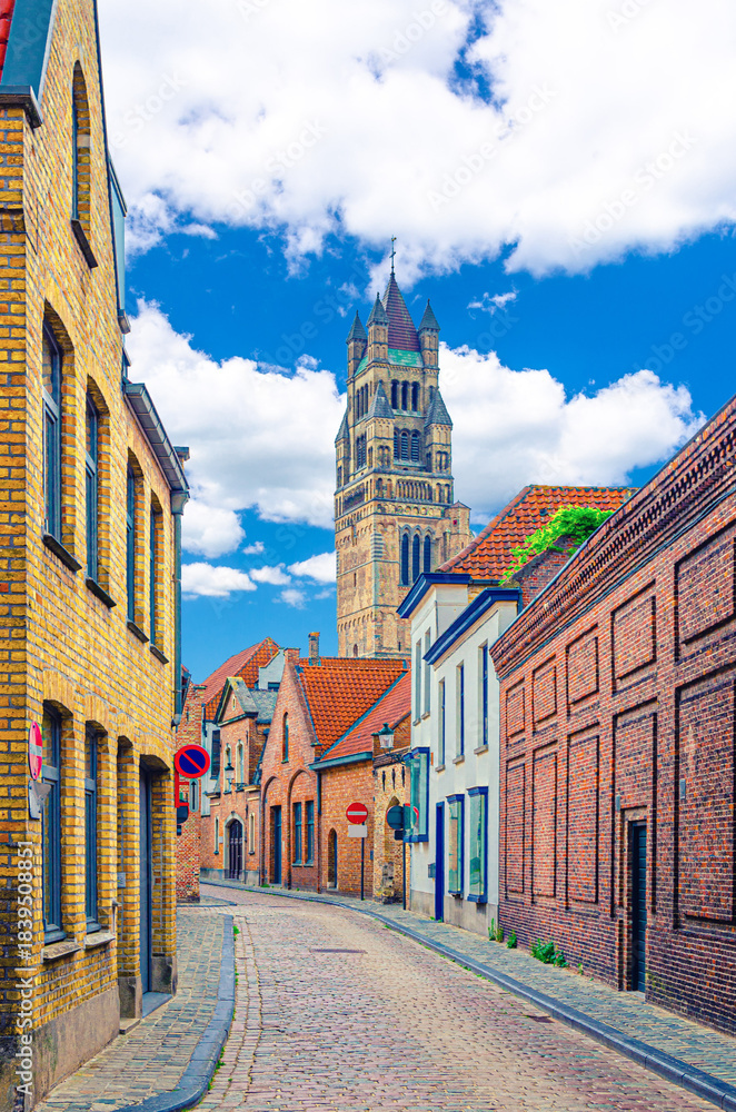 Obraz premium Bruges old town district, narrow cobblestone street, colorful buildings with brick walls in Brugge city historic center, St. Salvator's Cathedral tower, vertical view, West Flanders province, Belgium