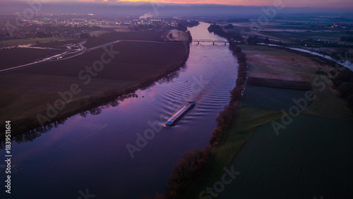 Ein Schiff fährt auf einem Fluss bei Sonnenuntergang in einer ländlichen Gegend