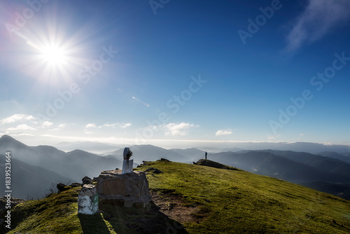 Bright sunstar over mountain summit viewpoint with distant misty valley, Hiker enjoying solitude