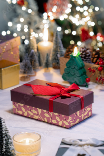 A pink gift box with red bow ribbon on table, Christmas festive decoration atmosphere and celebration ambiance with bokeh light illimitation in background.