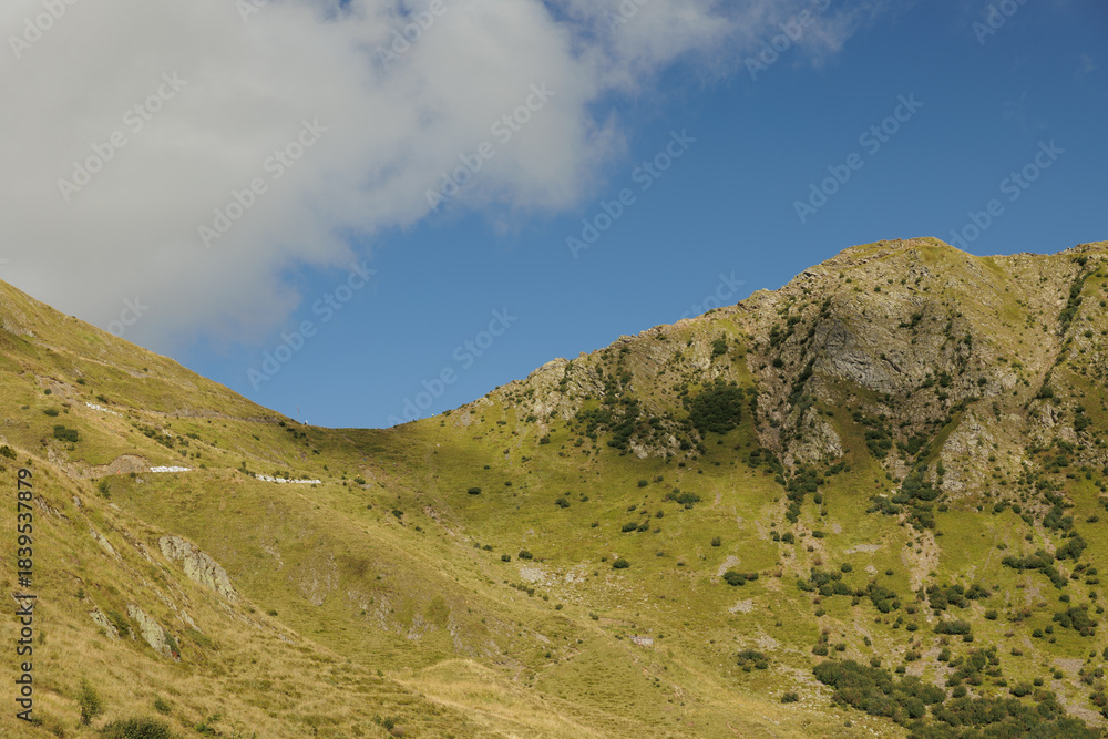 Fototapeta premium pendii e cime erbose di una catena montuosa verde, di giorno, in estate, con cielo azzurro, in Italia