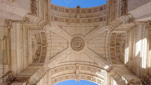Looking up at an ornate, arching stone ceiling against a clear, blue sky