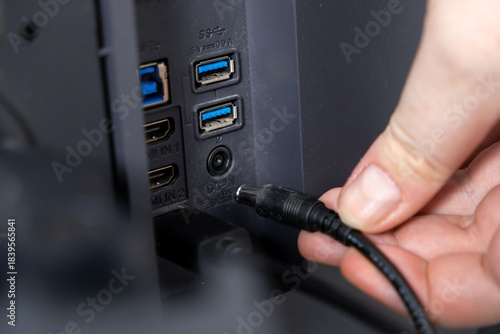 Tablou pe pânză User's hand plugging a black DC-IN power cable into the back panel of a modern e