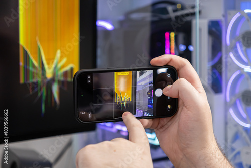 Person's hands film a broken computer monitor with a smartphone, documenting the glitched screen for technical repair and content creation