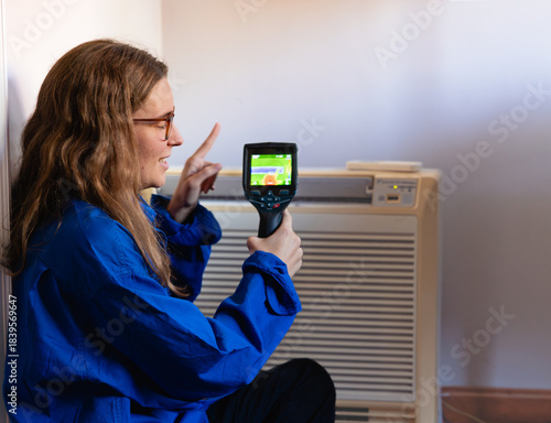Woman technician inspecting air conditioner with thermal camera
