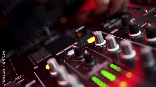 DJ performing in a club, close-up hand adjusting controls on a professional DJ mixer. Vibrant club lights, party atmosphere, music performance and nightlife vibes.