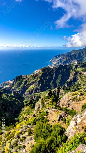 Lush green mountains meet a bright blue ocean under a partly cloudy sky in a picturesque, serene landscape