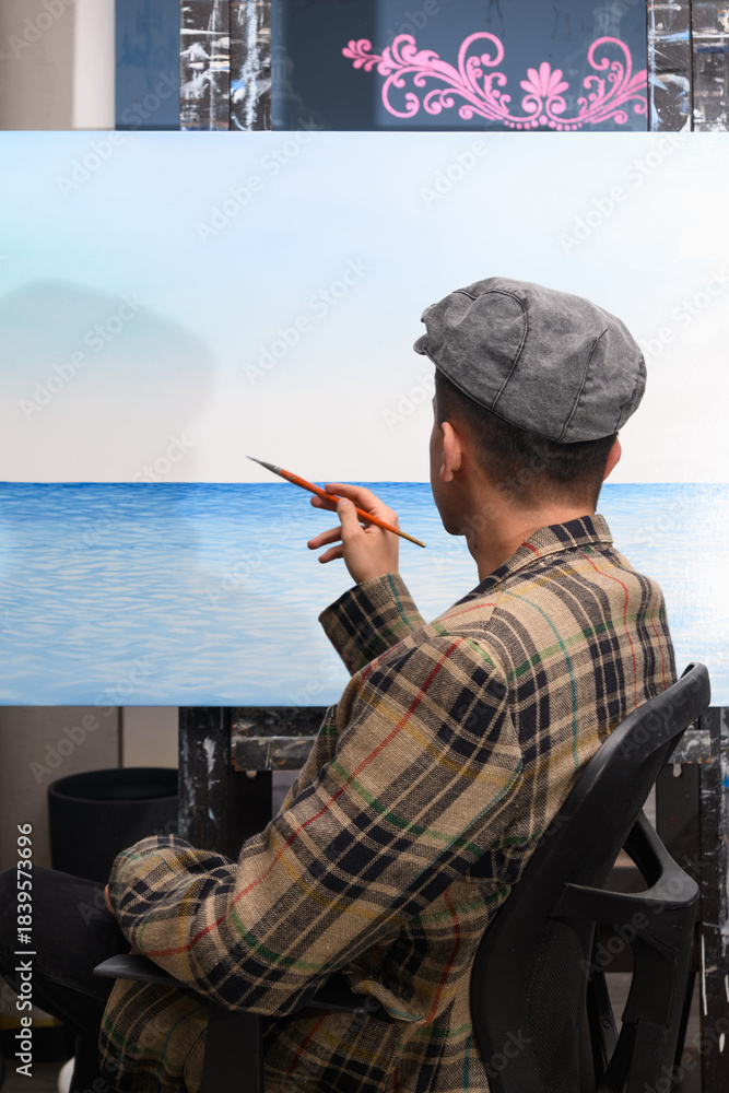 Obraz premium Male artist painting a seascape canvas, viewed from the back