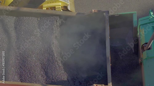 Hot steaming asphalt concrete being unloaded from a dump truck into a paver finisher machine
