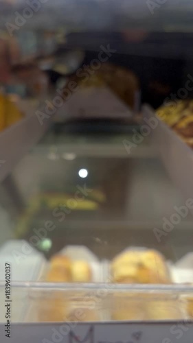 Bakery attendant taking a chocolate chip cookie with dulce de leche cream topping from the display.