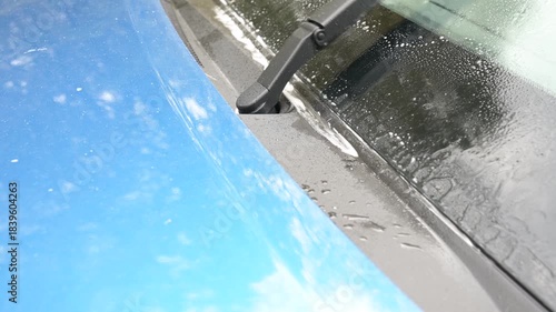 Close-up video of windshield washer jets spraying cleaning fluid onto a car windshield, with audible pump sound and water splashing on glass