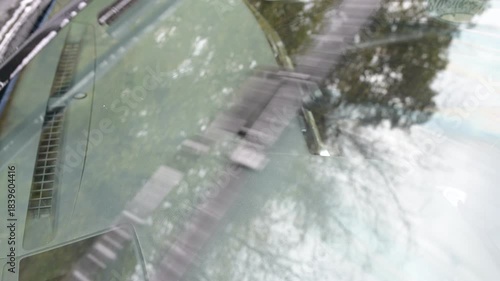 Front windshield wipers cleaning the glass, removing washer fluid and water streaks during operation, close-up view with natural ambient sound