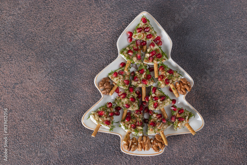 Appetizer of Brie cheese with pomegranate and walnuts in Christmas tree-shaped plate on brown background