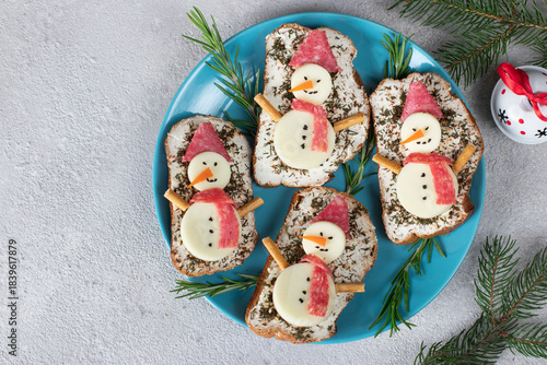 Sandwiches with mozzarella cheese and sausage, decorated with snowmen on blue plate