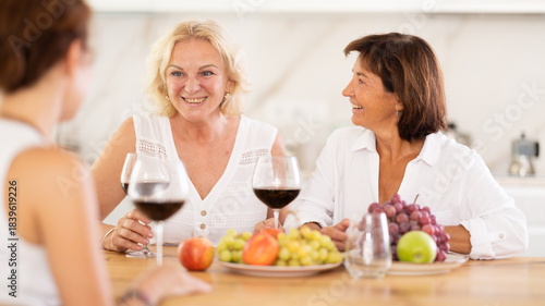 Girlfriends chatting and drinking wine at home party table in kitchen