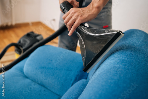 Bild auf Leinwand Close-up cropped shot of unrecognizable professional cleaning service worker removing dirt and stains from blue upholstered sofa using extraction washing vacuum cleaner in living room